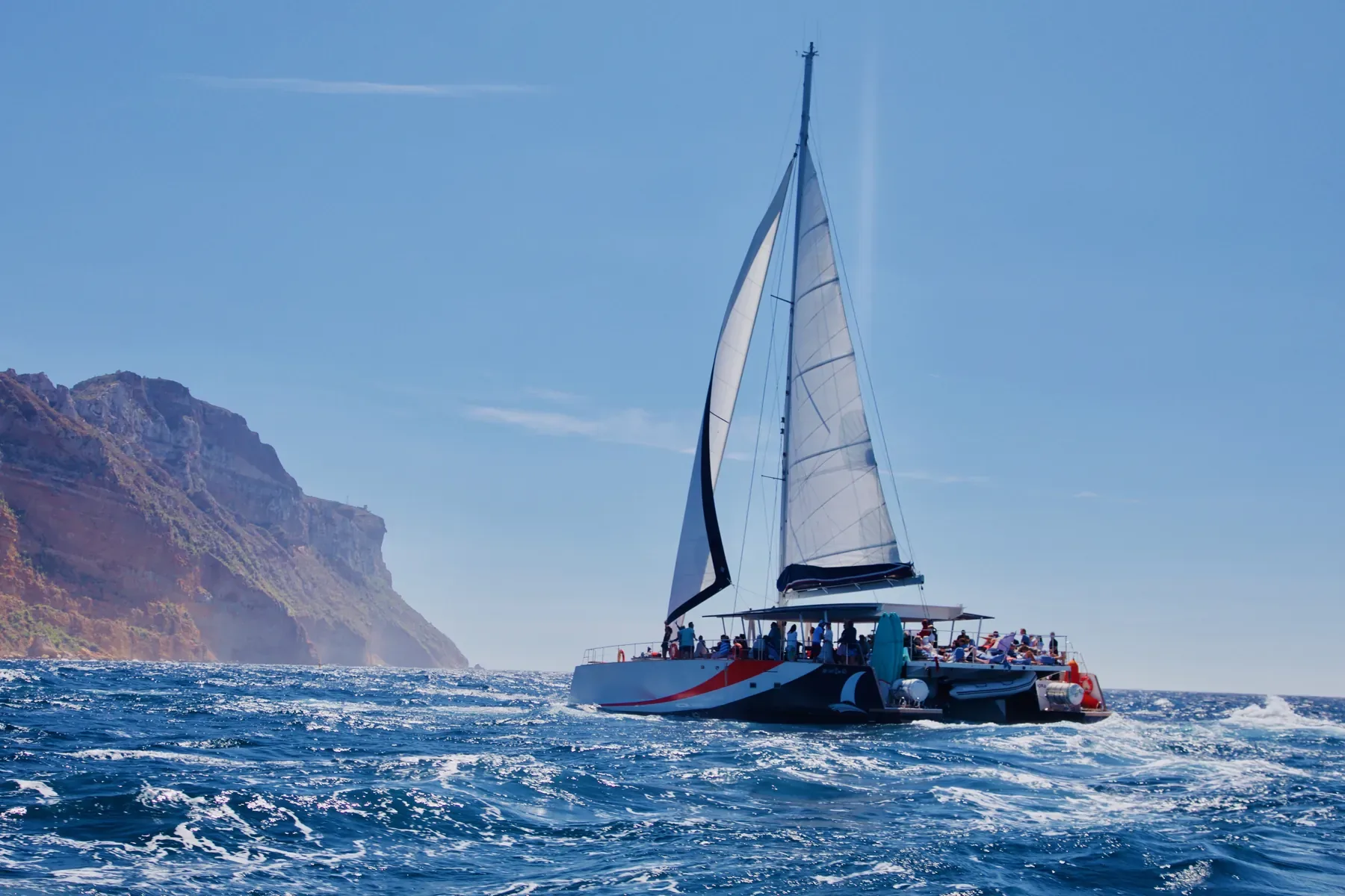 Un maxi-catamaran sous voiles devant le cap Canaille
