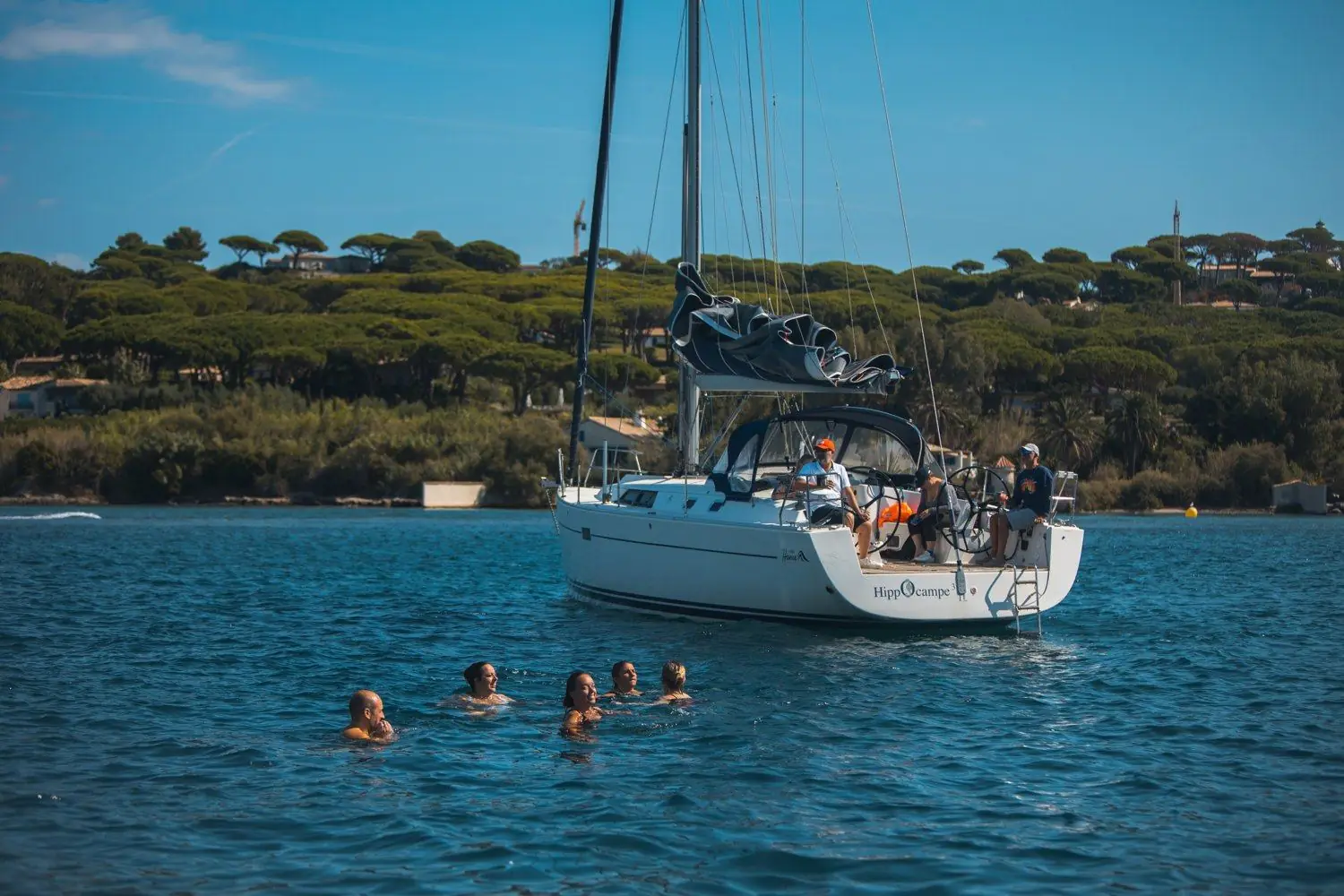 Voilier privatisé au mouillage devant une île, baigneurs dans l'eau