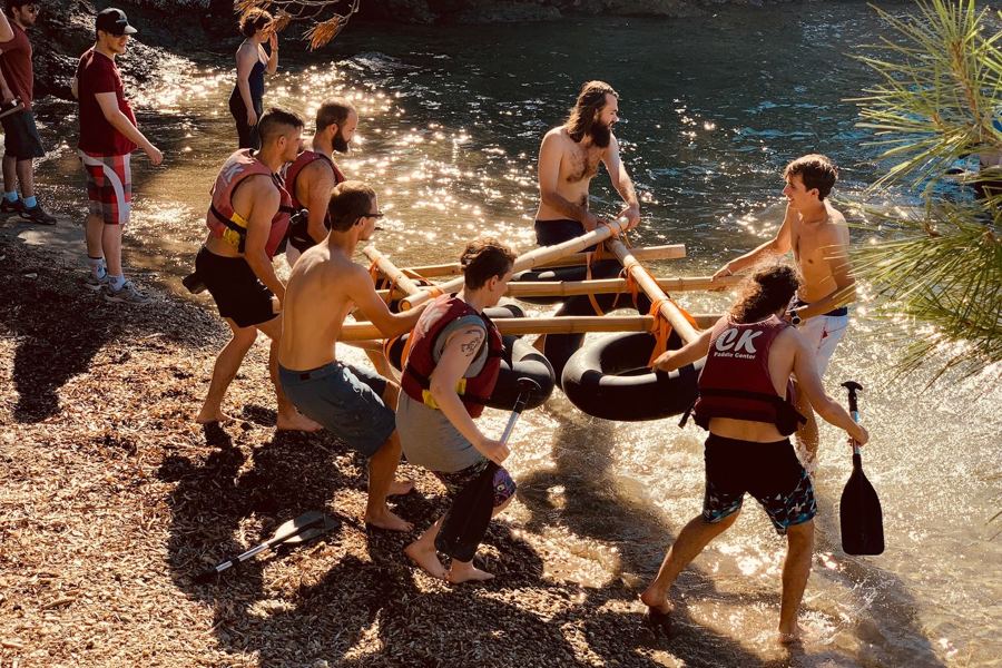 Équipes portant leur radeau jusqu'à l'eau, dans une crique bordée de pins