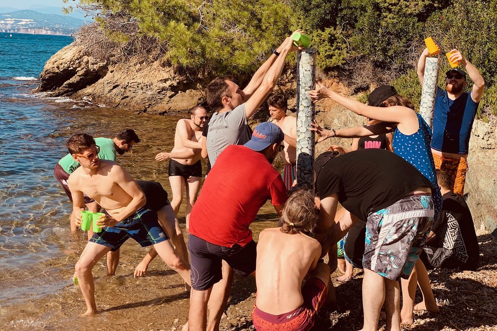 Équipes dressant leurs totems les pieds dans l'eau, au bord d'une crique