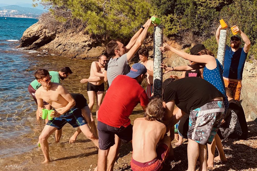 Équipes dressant leurs totems les pieds dans l'eau, au bord d'une crique