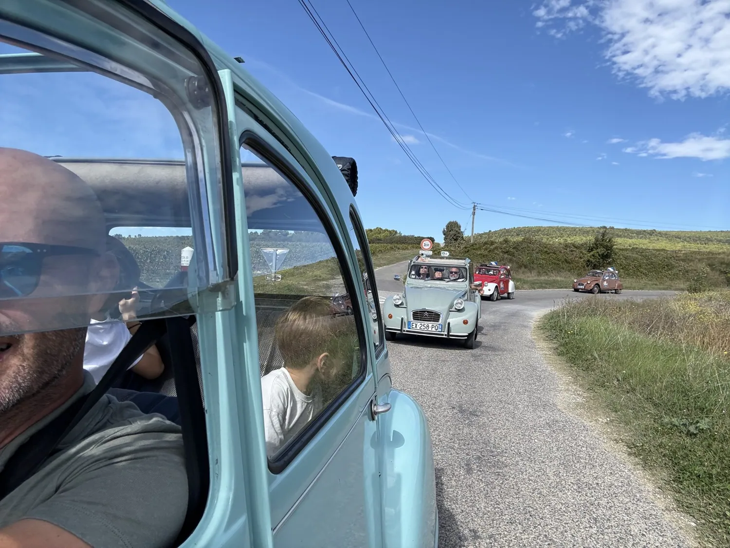 Le convoi de 2 CV vu depuis la banquette arrière d'une voiture
