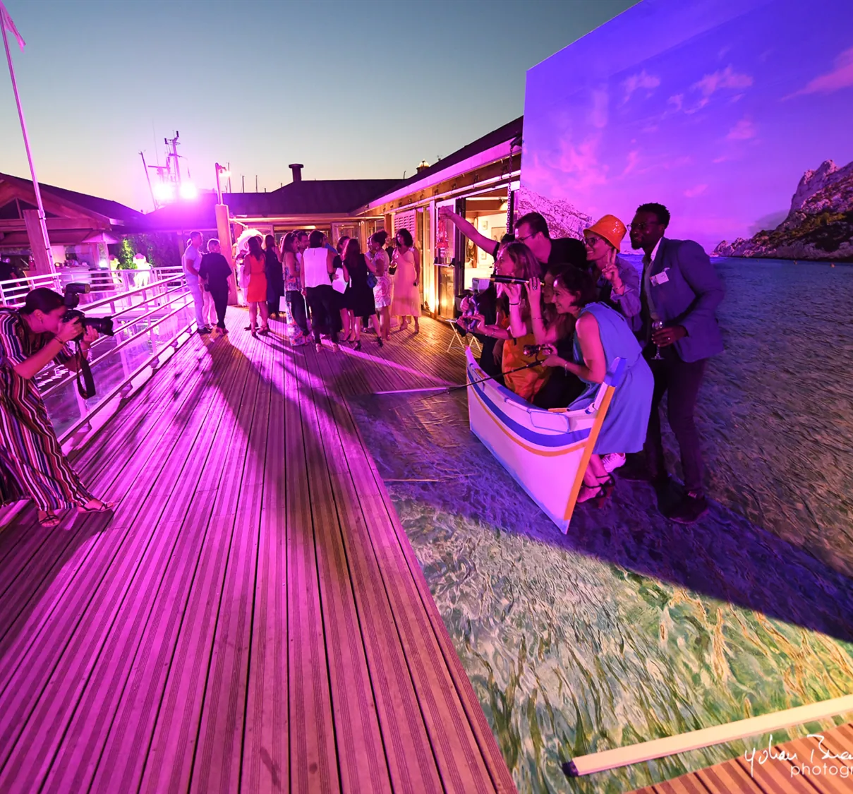 Une terrasse de bord de mer éclairée en soirée, les invités debout