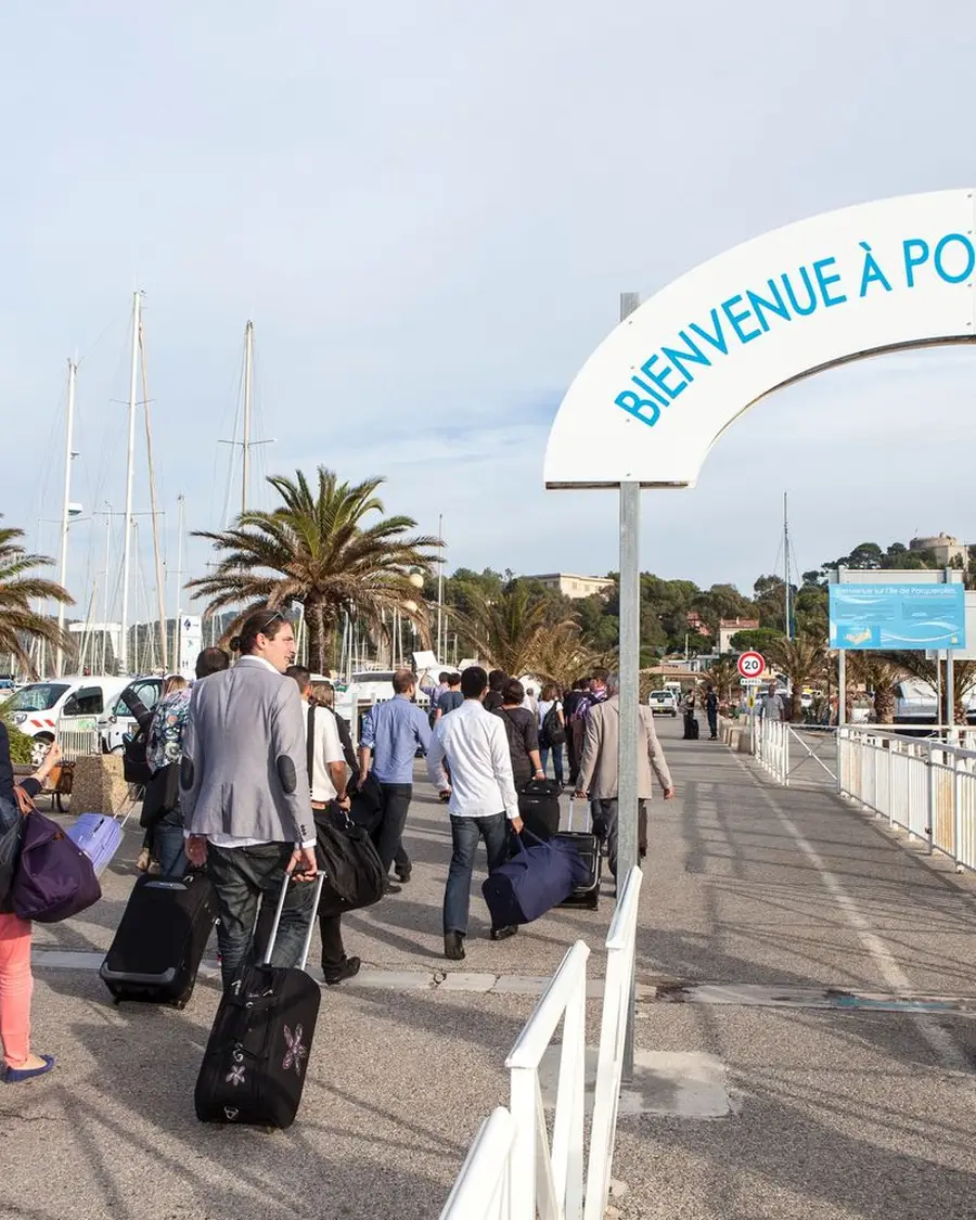 Arrivée d'un groupe à Porquerolles, valises à la main, sous l'arche de bienvenue