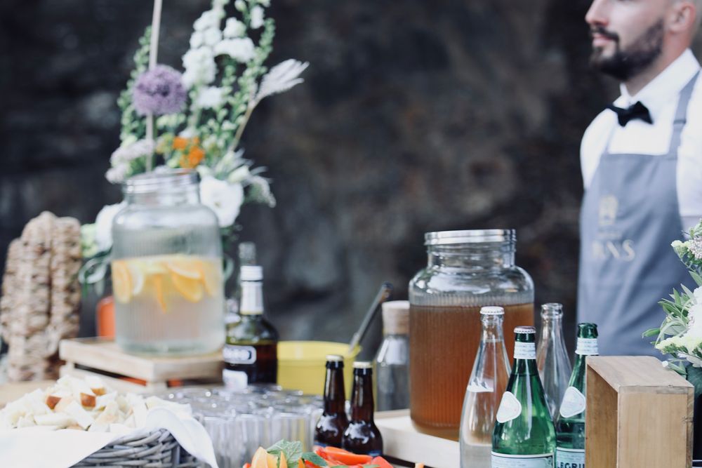 Bar à cocktails dressé avec fleurs et carafes, un serveur en tablier
