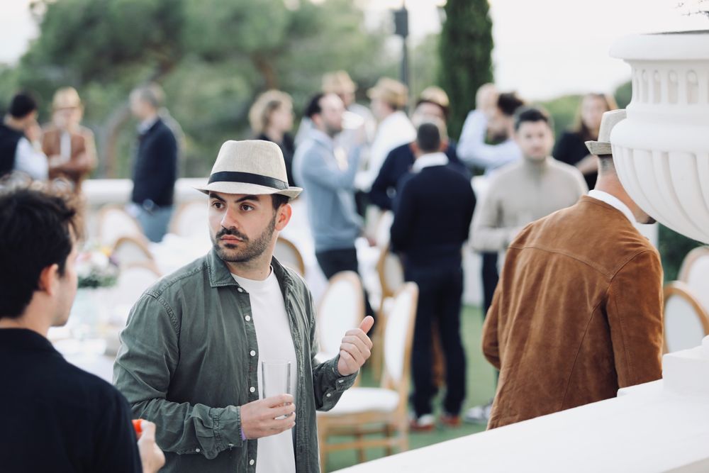 Invités qui discutent un verre à la main, sur une terrasse au milieu des pins