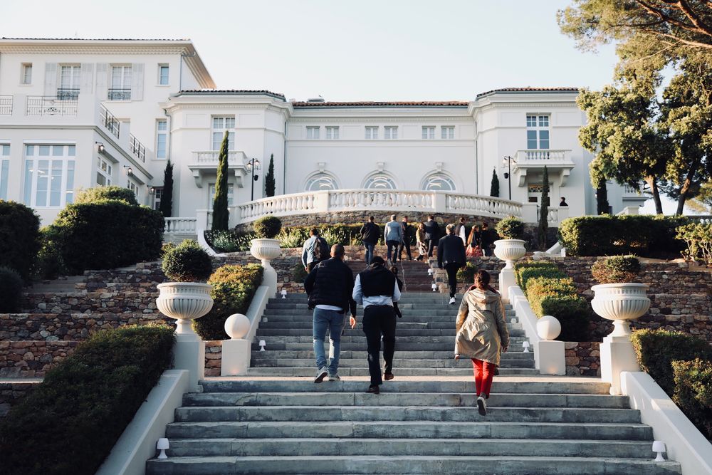 Invités montant le grand escalier d'une villa blanche, à l'arrivée