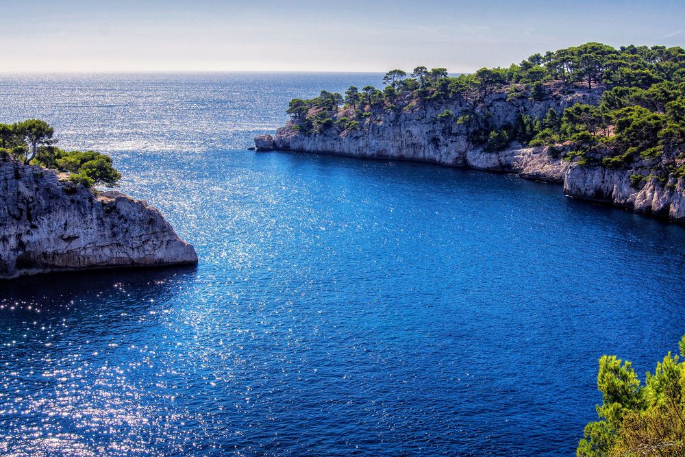 Eau bleue entre deux falaises boisées, dans une calanque