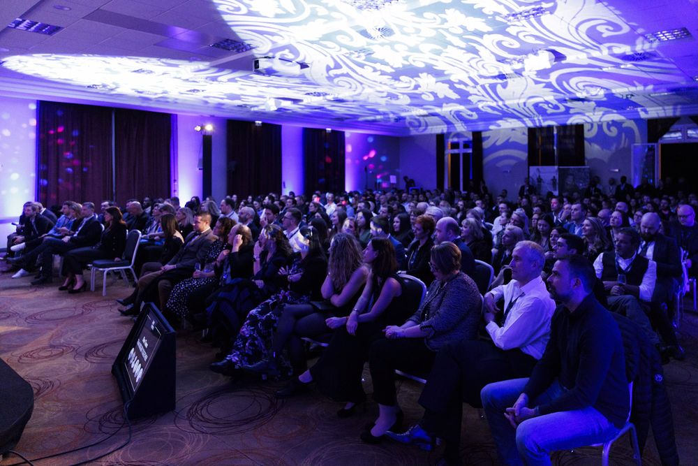 Grande salle plénière sous une lumière violette, les participants tournés vers la scène