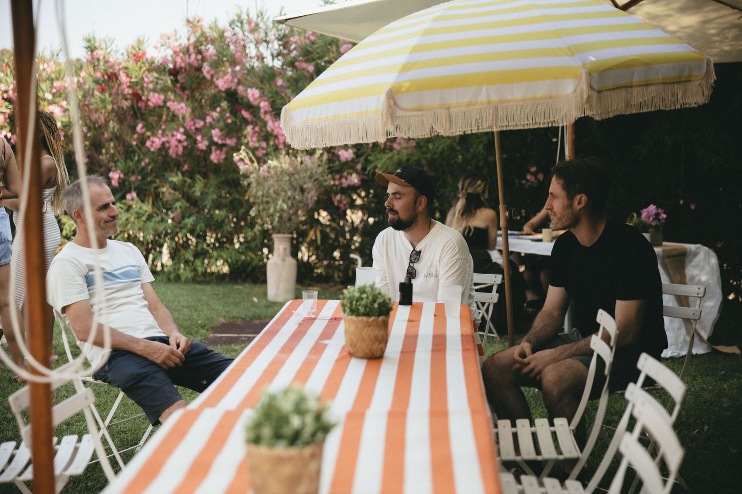 Petit groupe en discussion autour d'une table rayée, sous un parasol