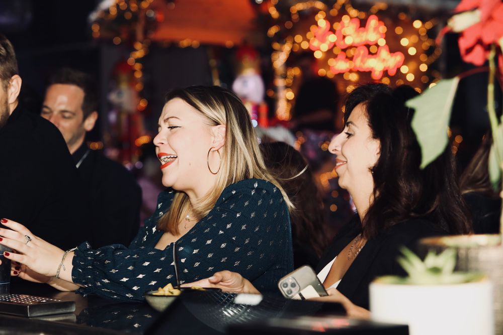 Invitées qui rient au bar, devant le chalet de Noël illuminé