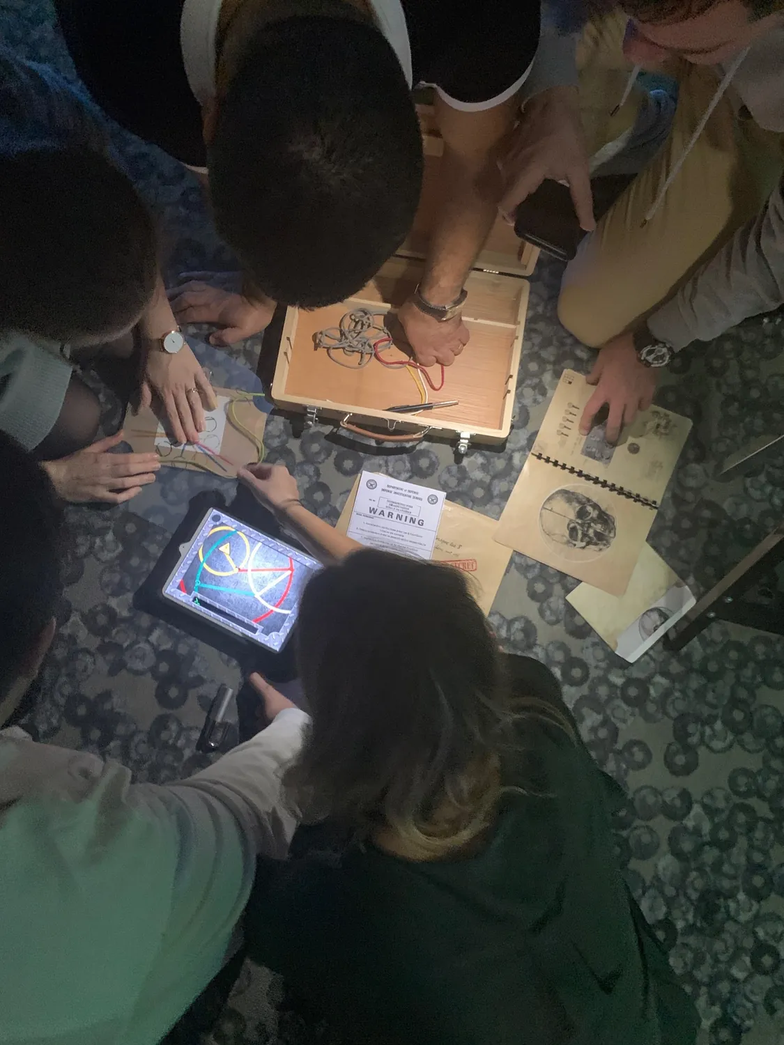 Vue de dessus : la tablette, les documents du jeu et les indices étalés sur la table